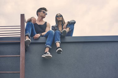 Çatıda oturan güneş gözlüğü Interracial genç çiftin alttan görünüm