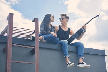 Akustik gitar ile çatıda oturan mutlu çok kültürlü çift