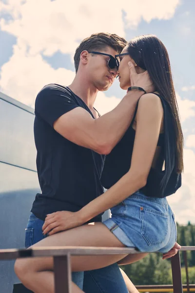 multiethnic hot couple going to kiss while sitting on railings on roof