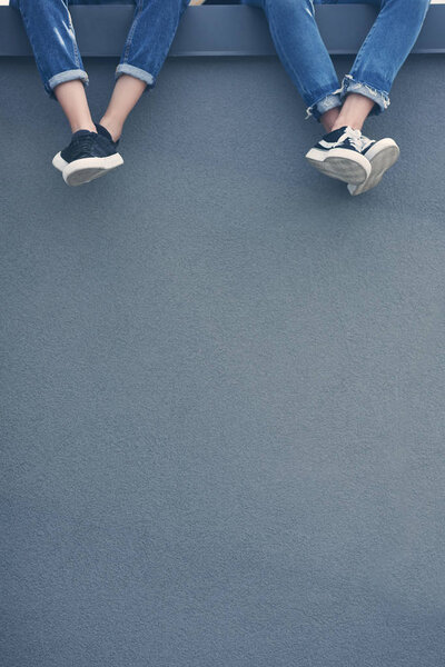 cropped view of couple in jeans and sneakers sitting on grey wall