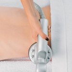 Delvis skymd utsikt över kvinnan på massagebänk får elektrisk massage utförs av kosmetolog i spasalong