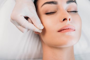 partial view of cosmetologist putting needle on womans face during acupuncture therapy in spa salon clipart