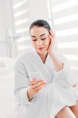 beyaz bornoz spa salonda smartphone kullanarak kadın portresi