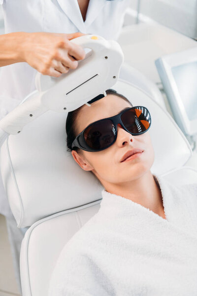 woman in protective eyeglasses getting laser hair removal made by cosmetologist in spa salon