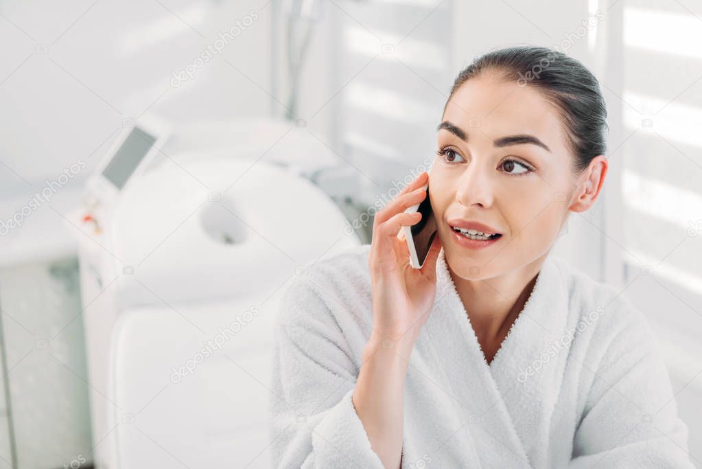 portrait of woman in white bathrobe talking on smartphone in spa salon