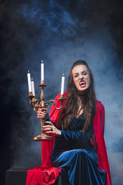 vampire woman holding antique candelabrum on darkness with smoke 