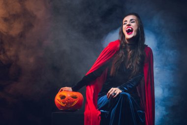 Vampir kostümü duman ile koyu arka plan üzerinde gülümseyen güzel kadın 