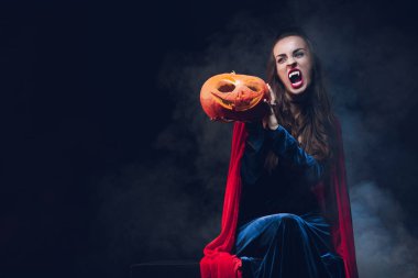 Vampir kostümü kabak duman ile koyu arka plan üzerinde tutan kadın 