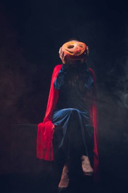 kırmızı pelerini jack o fener yüz duman ile koyu arka plan üzerinde önünde tutan kadın 