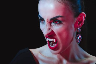 dreadful vampire showing her fangs and looking away isolated on black clipart