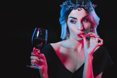 bardağı kan ile tutarak ve siyahta izole parmaklarını yalama vampir kadın