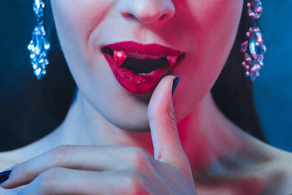 cropped view of vampire with bloody lips and fangs