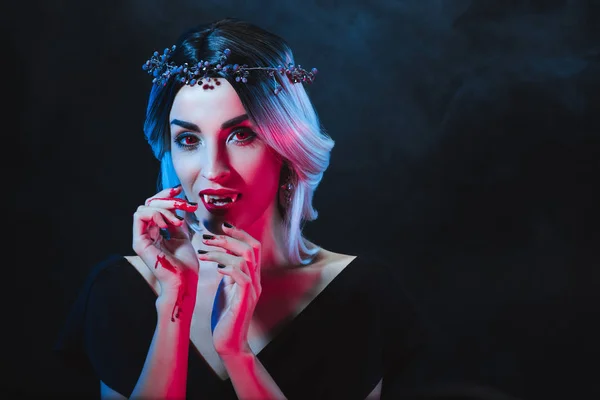 mystic woman showing vampire teeth on dark background with smoke