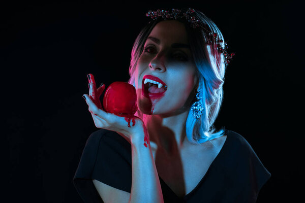 attractive vampire woman bitting red bloody apple isolated on black