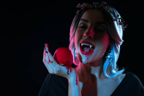 mystic vampire woman bitting red bloody apple isolated on black