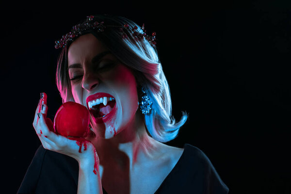 sexy vampire woman bitting red bloody apple isolated on black