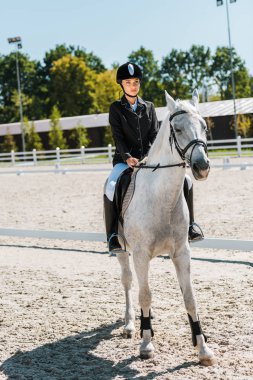 attractive female jockey riding horse at horse club clipart