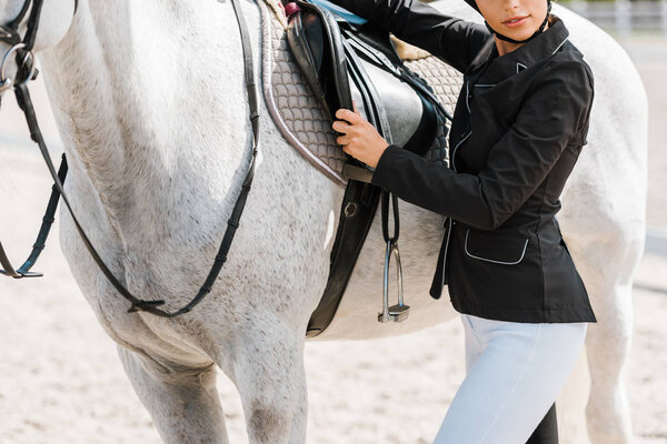 cropped image of female equestrian fixing horse saddle at horse club