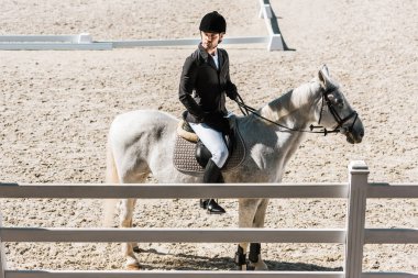 yakışıklı erkek Equestrian sınıftan at çiftliği nde oturan ve uzak seyir profesyonel Konfeksiyon yan görünüm
