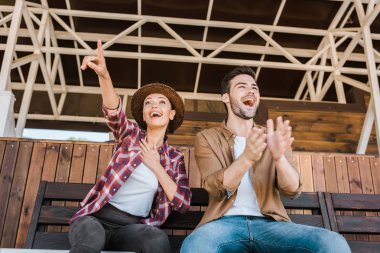 excited fans in casual clothes sitting on bench at ranch stadium and watching horse races clipart