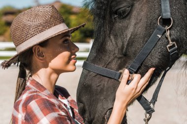 portrait of attractive female equestrian touching and looking at horse at ranch clipart