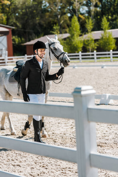 smiling handsome male equestrian walking near horse at horse club