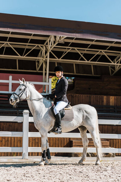 side view of handsome male jockey riding horse at horse club