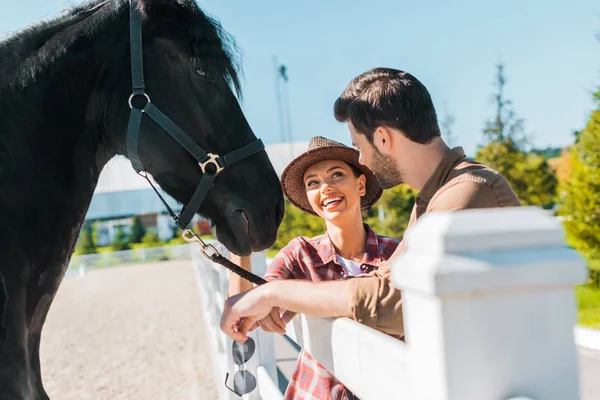 カウボーイとカウガールの牧場で馬の近くに立って お互いを見て笑みを浮かべてください — ストック写真