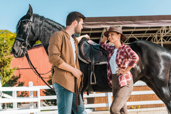 low angle view of female and male equestrians standing near horse and talking at ranch 