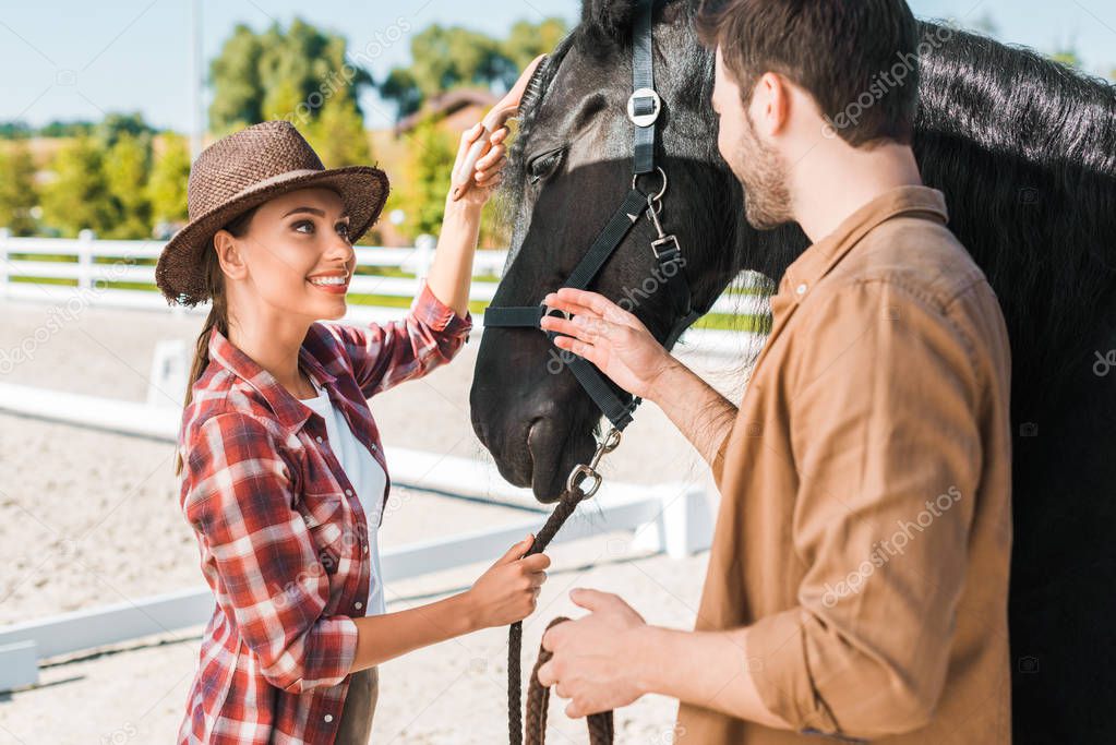 cheerful cowboy and cowgirl looking at each other near horse at ranch