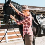Cowgirl atraente fixação halter cavalo no rancho e olhando para a câmera