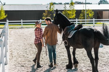 back view of cowboy and cowgirl walking with horse at ranch clipart