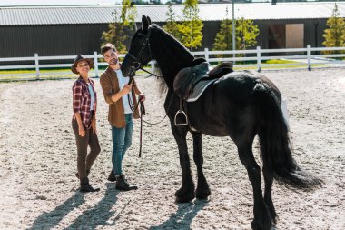 smiling female and male equestrians standing with horse at ranch clipart