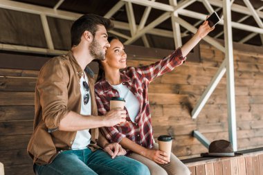 Selfie ile smartphone alarak ve ranch at kağıt bardak kahve holding gülümseyen iş arkadaşları