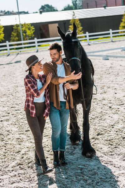 happy female and male equestrians walking with horse at ranch