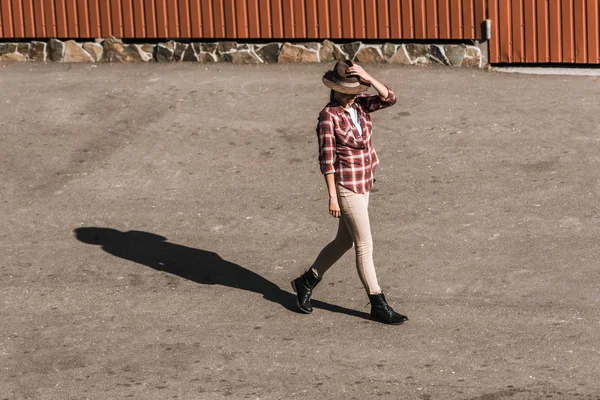 Atractiva Mujer Camisa Cuadros Tocando Sombrero Caminando Cerca Edificio Marrón —  Fotos de Stock