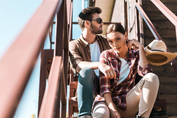 cowboy and cowgirl in casual clothes sitting on staircase at ranch