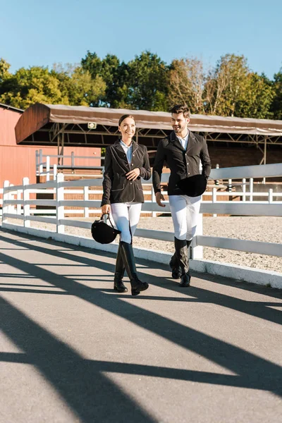 male and female equestrians in professional apparel walking near fence at ranch