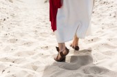 Oříznout obrázek Ježíše v roucho, sandály a červenou šerpou chůzi na písku v poušti