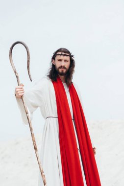 Jesus with long hair standing with wooden staff in desert clipart
