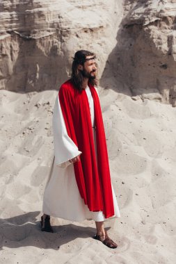 side view of Jesus in robe, red sash and crown of thorns walking in desert clipart