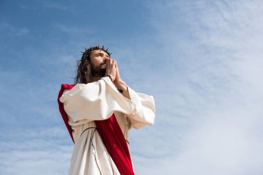 low angle view of Jesus praying against blue sky clipart