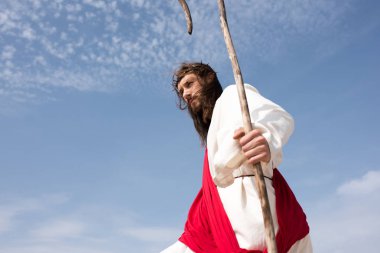elbise, kırmızı kuşak ve bulutlu gökyüzü karşı personel ile ayakta dikenli taç İsa'nın düşük açılı görünüş