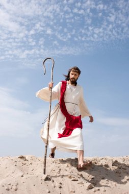 Elbise, kırmızı kuşak ve personel ile çölde yürürken dikenli taç İsa