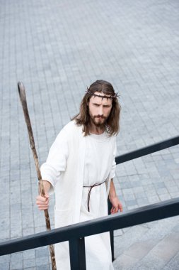 high angle view of Jesus in robe and crown of thorns standing on stairs with staff clipart