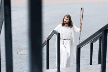 high angle view of Jesus in robe and crown of thorns walking on stairs with staff clipart