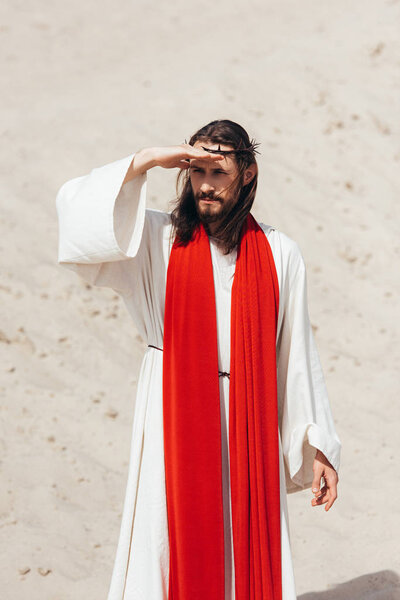 Jesus in robe, red sash and crown of thorns looking away in desert