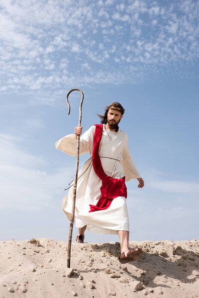 Иисус в мантии, красной ленте и терновом венце, идущем по пустыне с посохом
