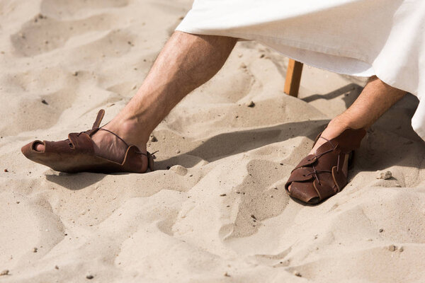 cropped image of Jesus in robe and sandals sitting on sun lounger in desert