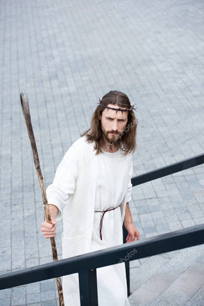 high angle view of Jesus in robe and crown of thorns standing on stairs with staff